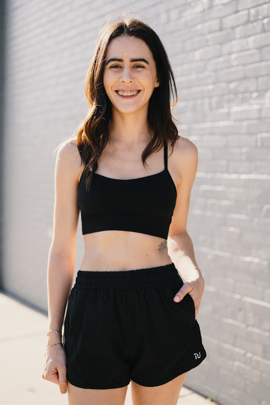 A person stands confidently in a black crop top and shorts, showcasing a sporty and trendy style.